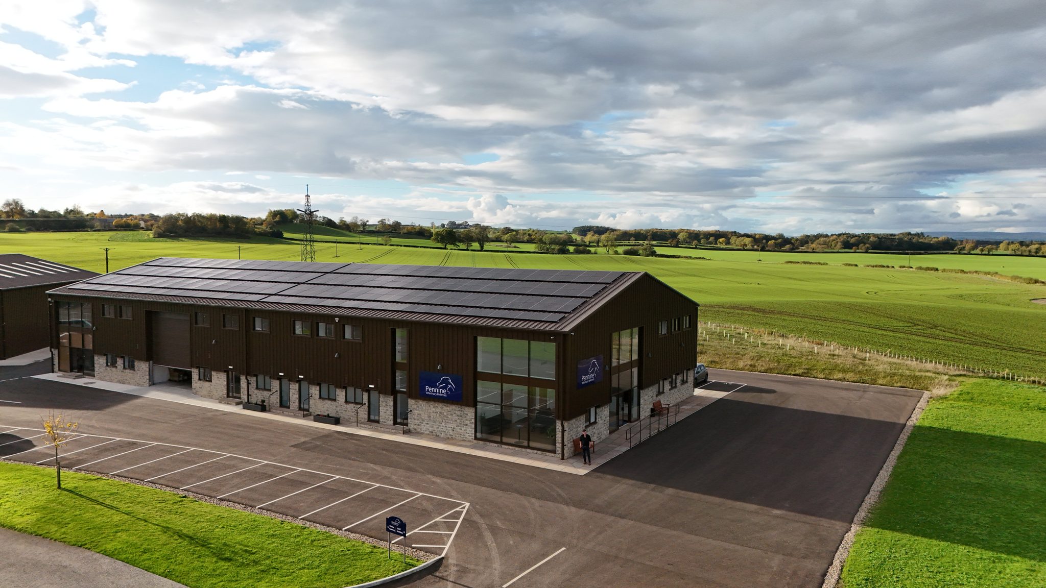 Pennine Veterinary Referrals — the completed building, timber cladding on a stone base with a glazed corner entrance and solar panels, in open North Yorkshire farmland